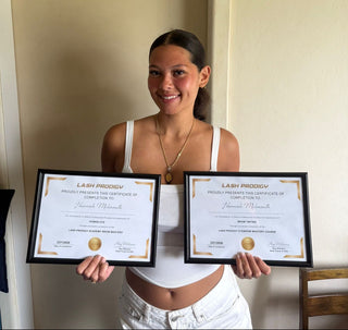 Woman holding two framed certificates in a room with a neutral background