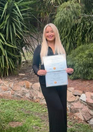 Person holding a certificate outdoors with greenery in the background